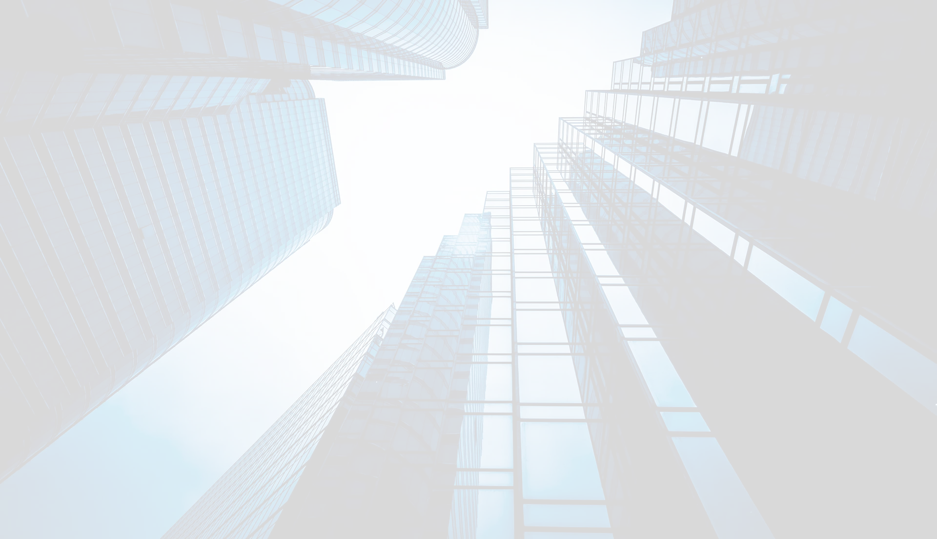Glass skyscrapers rise toward a bright sky, viewed from the ground looking up, reflecting light and nearby buildings.